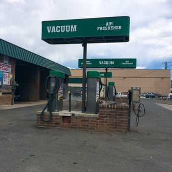 Vacuum station at a car wash, with green signs and brick base. Grey vacuums and hoses stand ready.