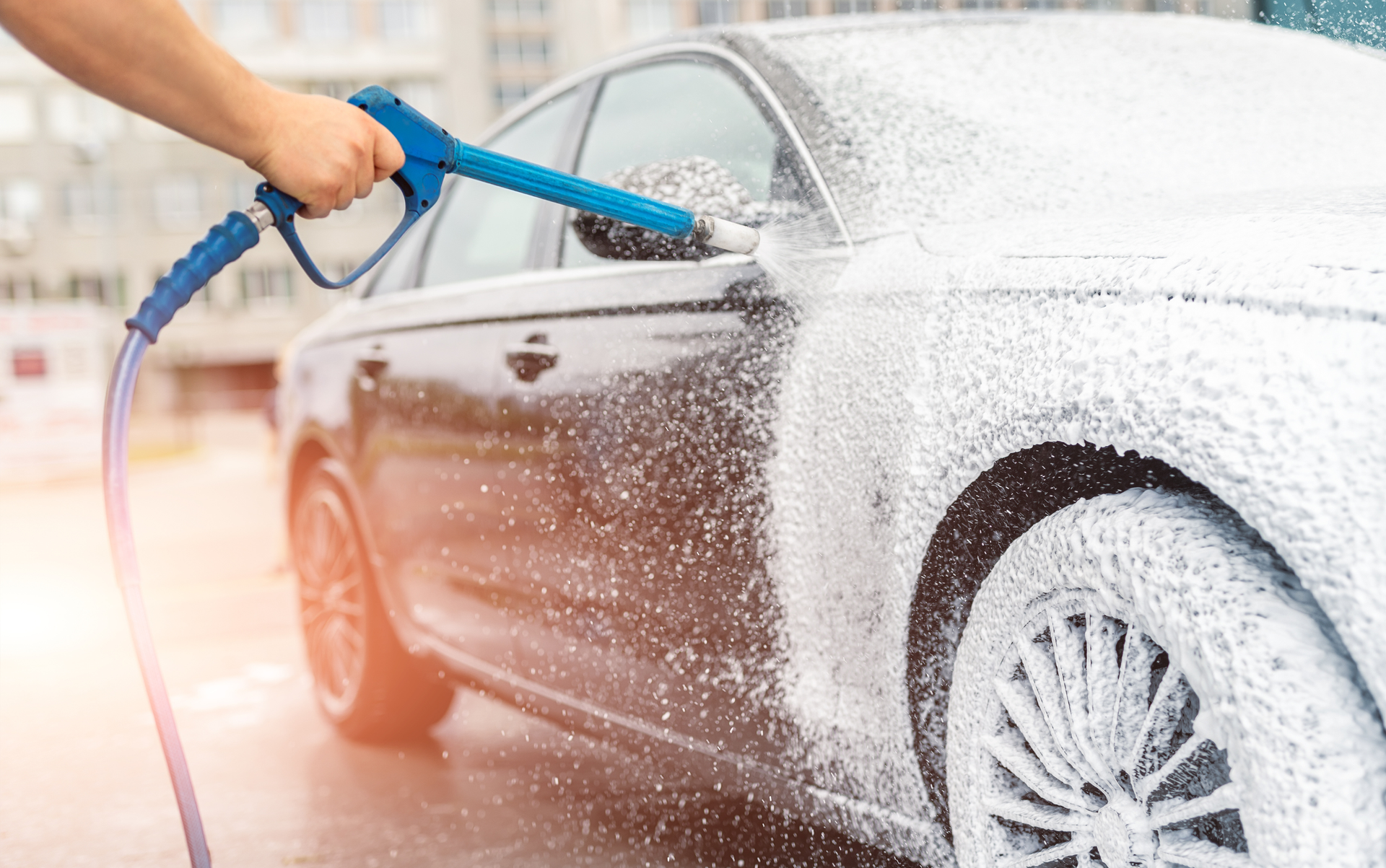 Hand spraying soapy foam on a black car.