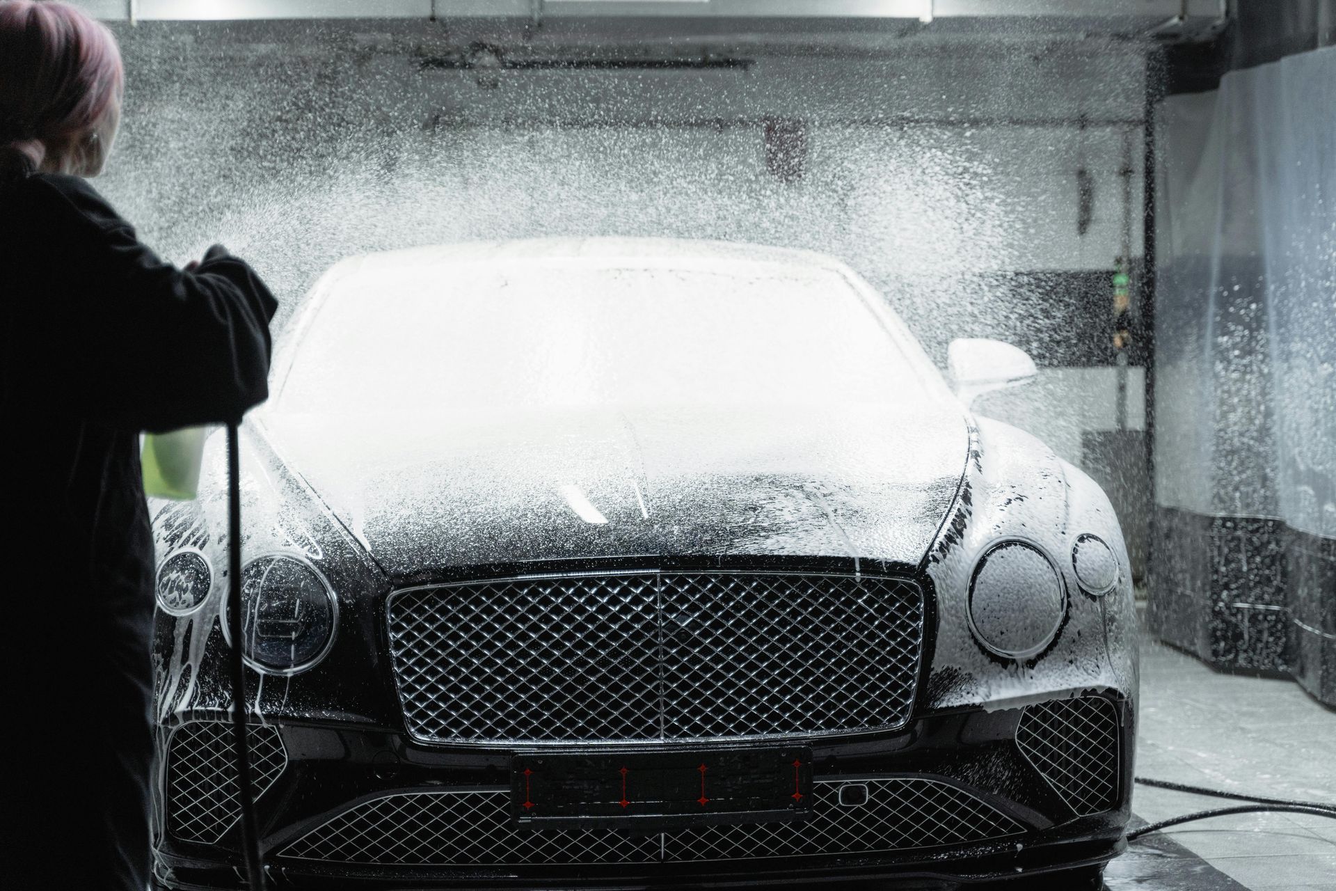 Person washing a black Bentley with soapy water at a car wash.
