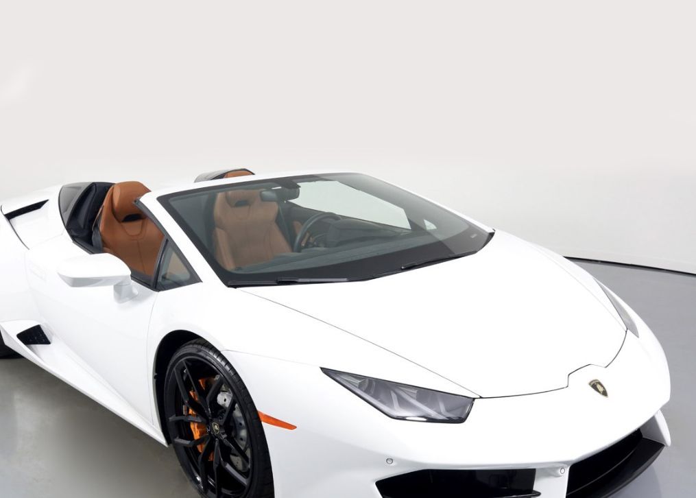 A white Lamborghini Huracan convertible is parked on a showroom floor.