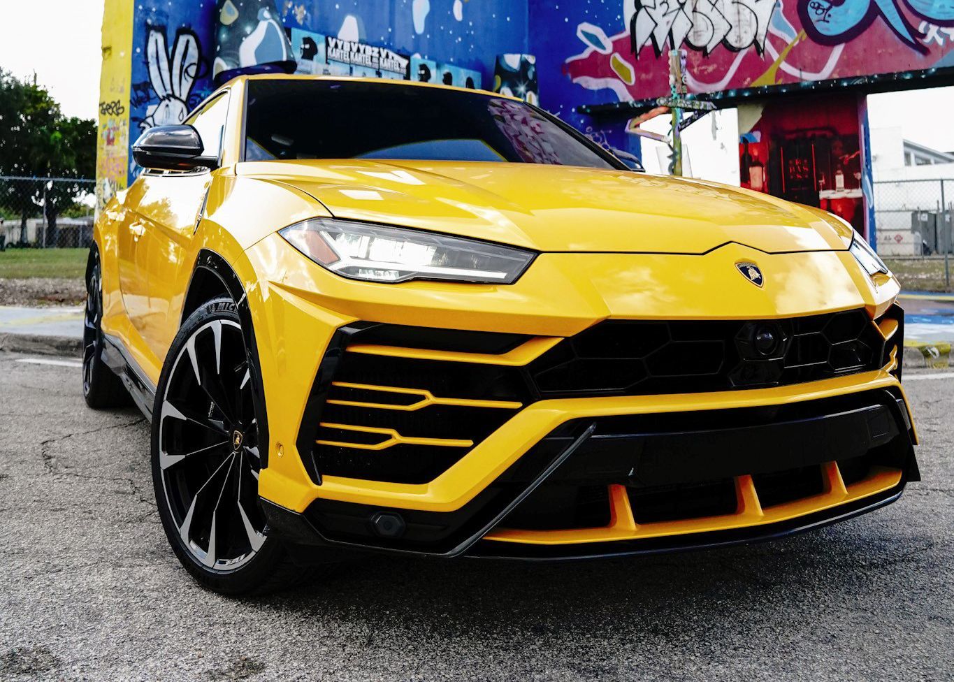 A yellow Lamborghini Urus is parked in front of a graffiti covered building.