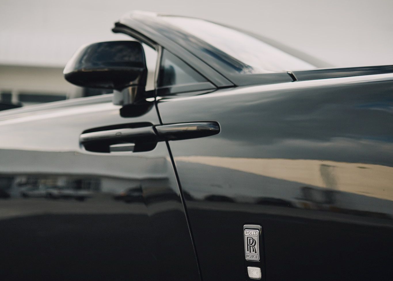 A black Rolls Royce car is parked in a parking lot.