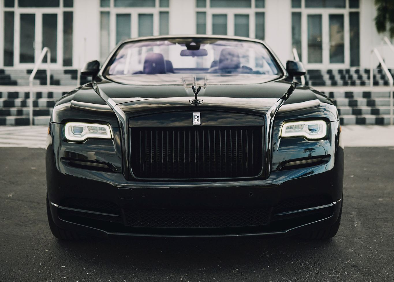 A black Rolls Royce is parked in front of a building.