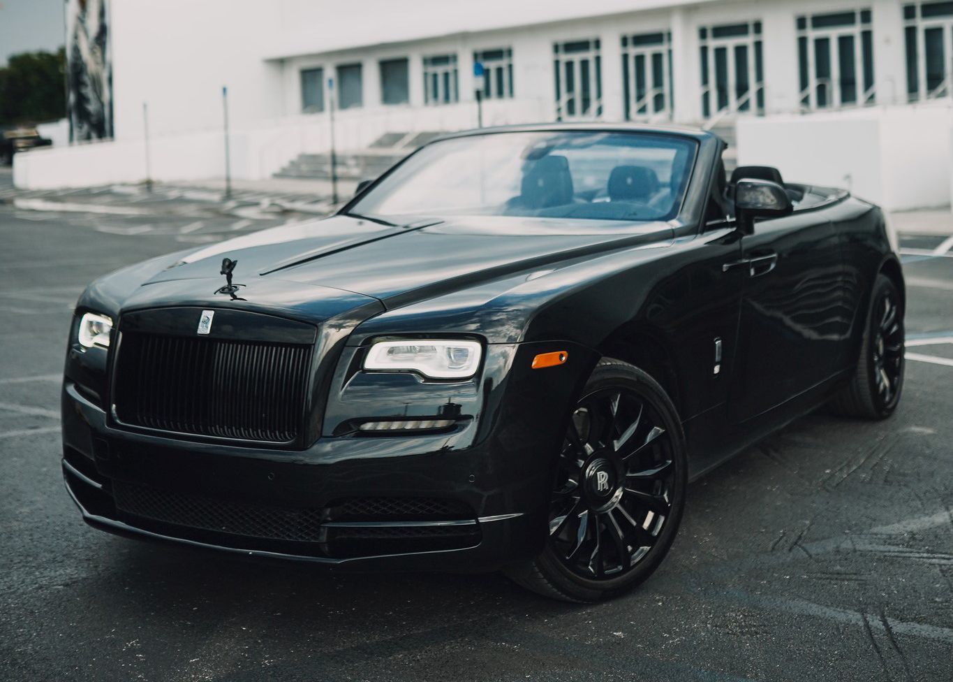 A black Rolls Royce convertible is parked in a parking lot.