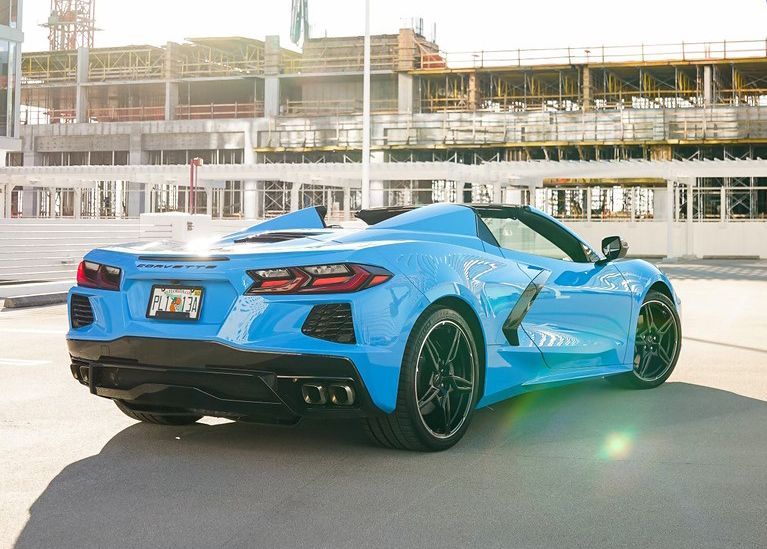 A blue sports car is parked in a parking lot in front of a building under construction.