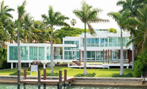 A large white house is surrounded by palm trees next to a body of water.