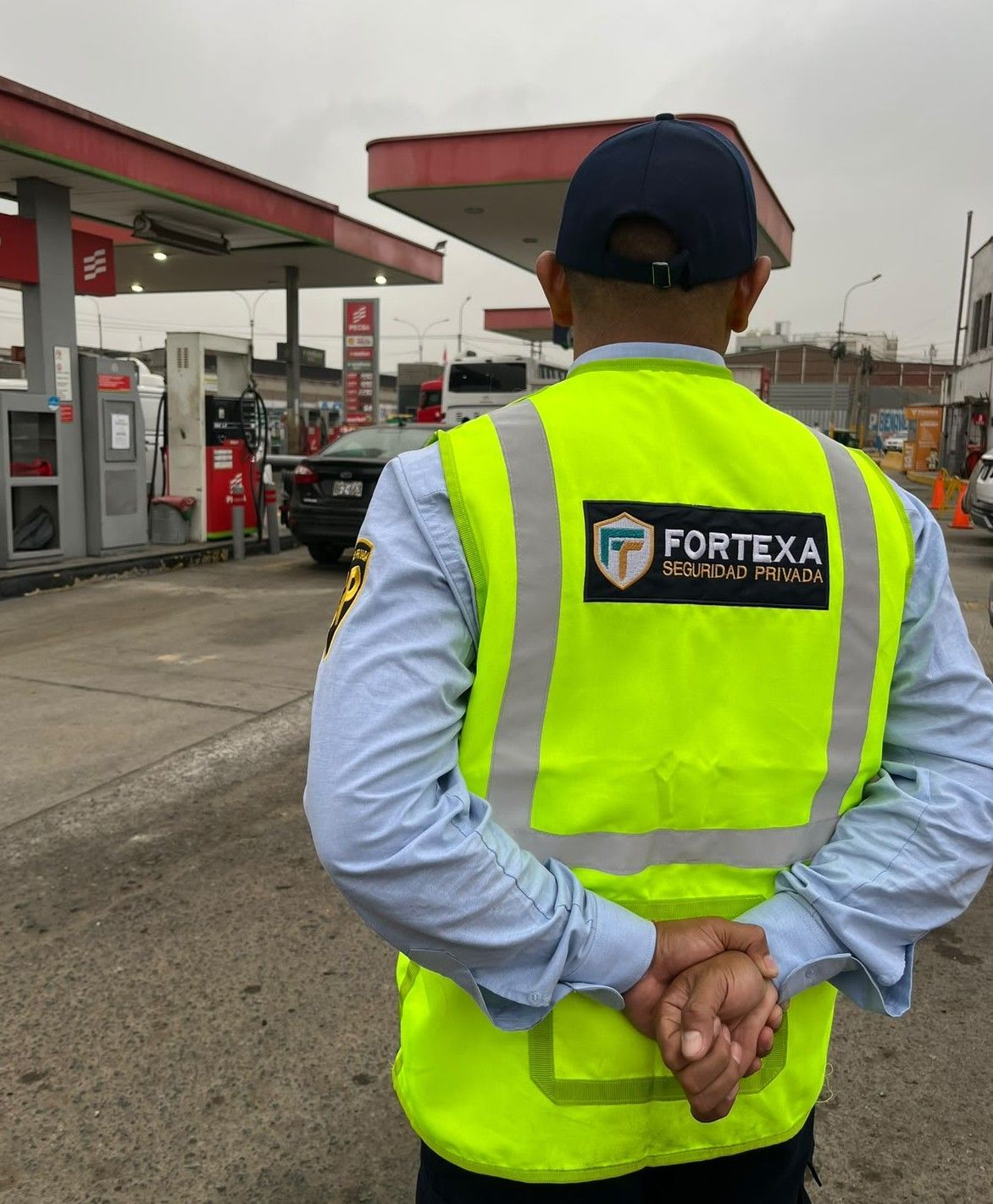 Un trabajador con chaleco reflectante de seguridad está de pie en una gasolinera con las manos detrás de la espalda.