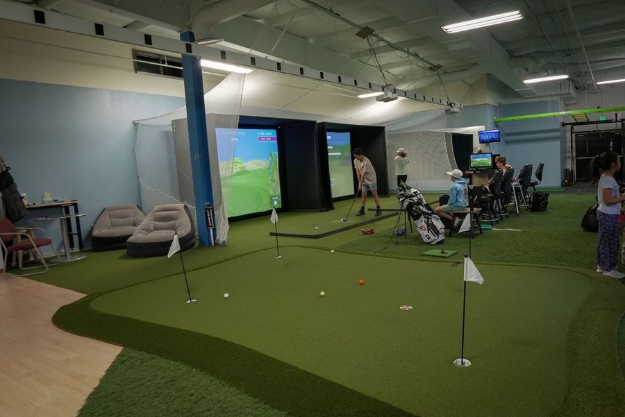 Indoor golf facility with putting green, simulators, and people playing.