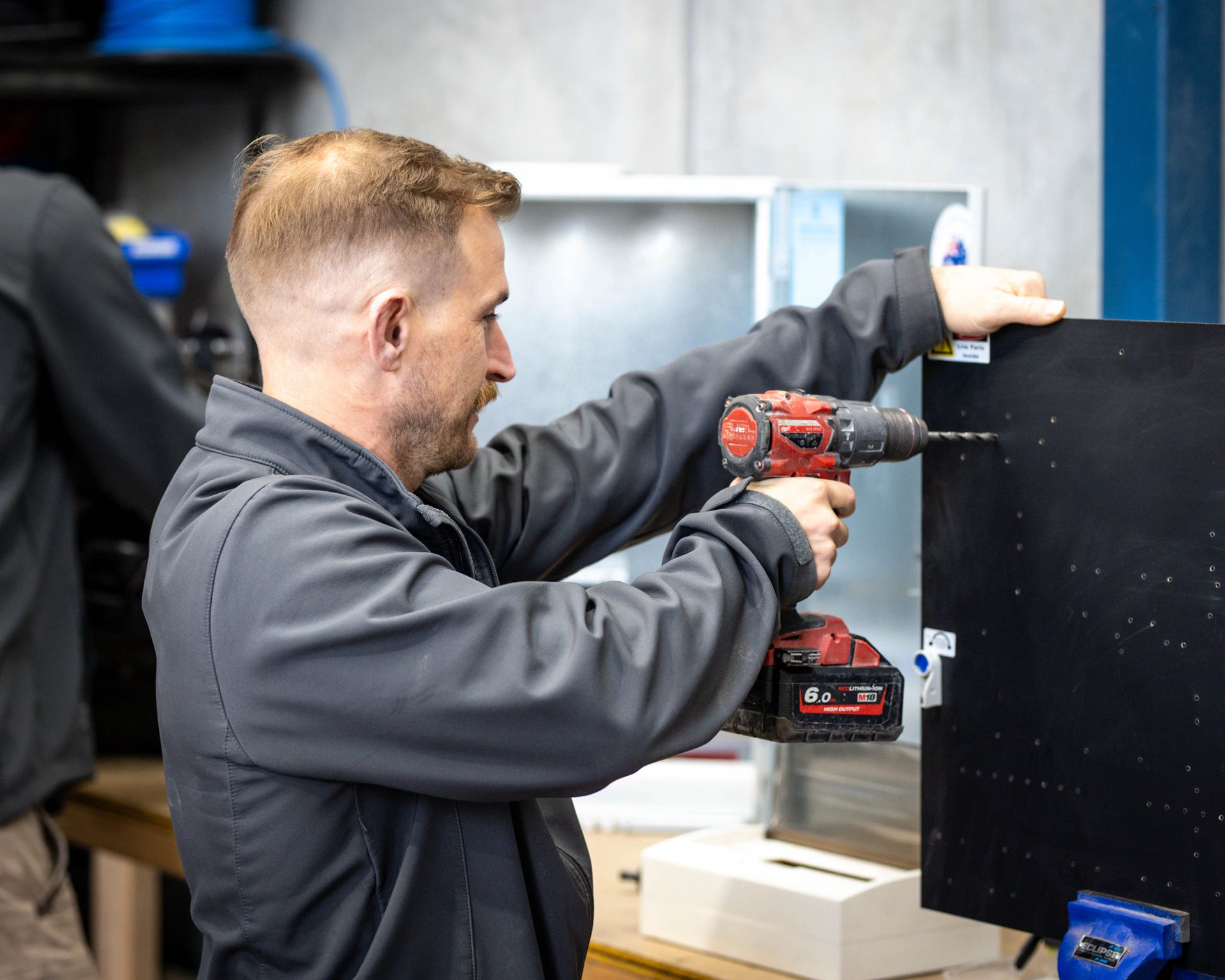 Worker using a red drill to install a black panel in a workshop