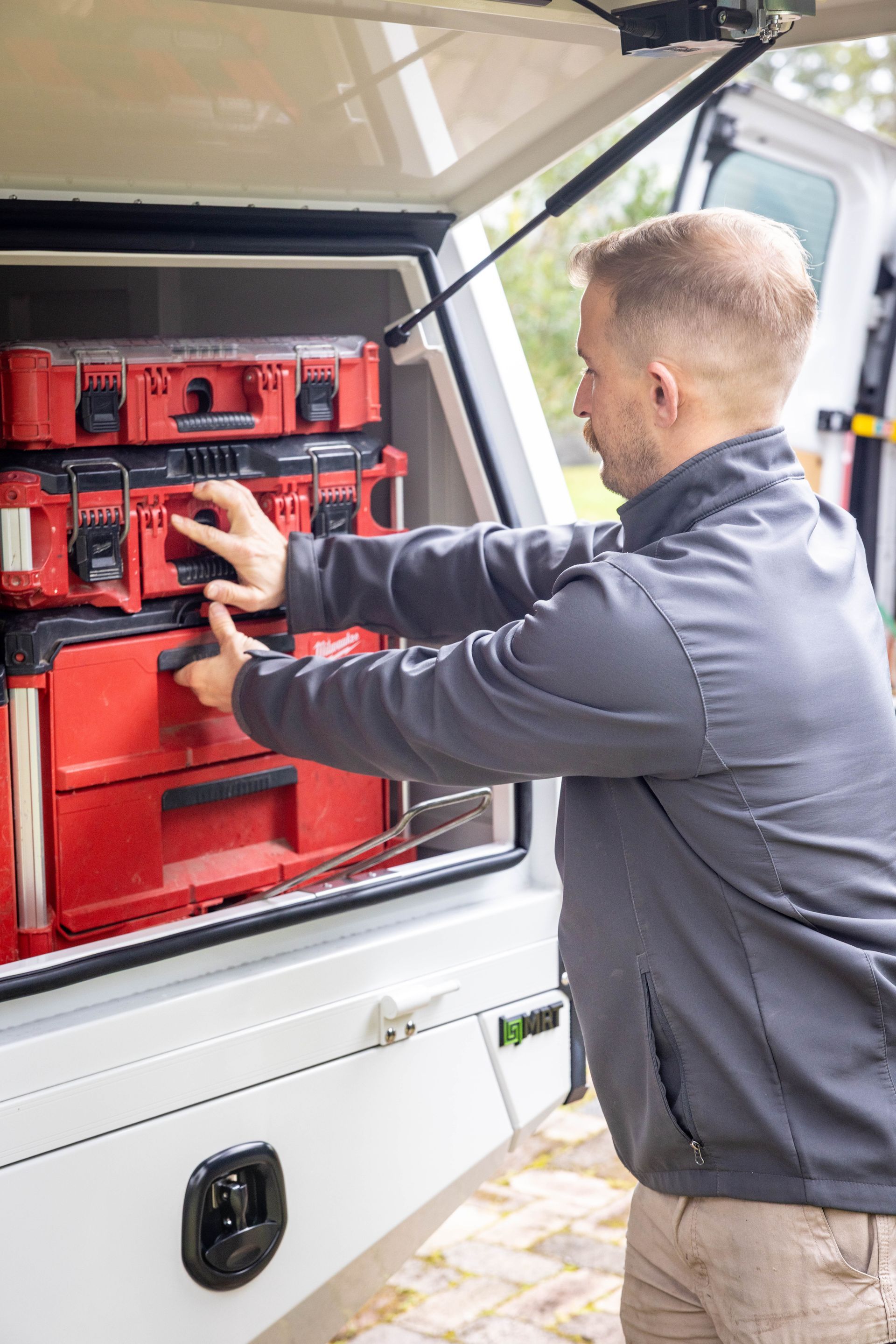 Man organizing red tool cases in an open van trunk