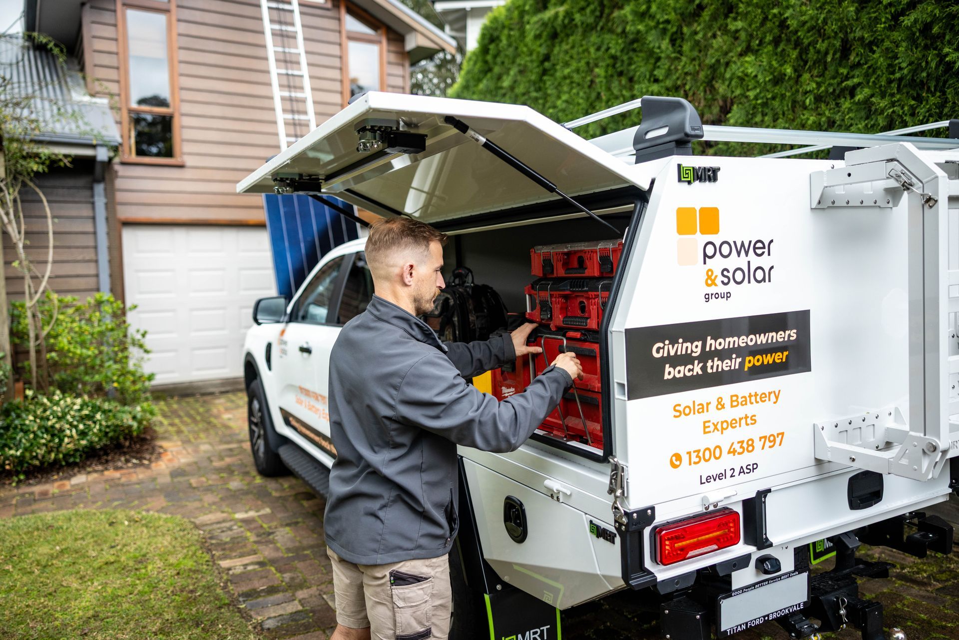Worker loading red batteries into a white Powerwall Solar truck in a driveway