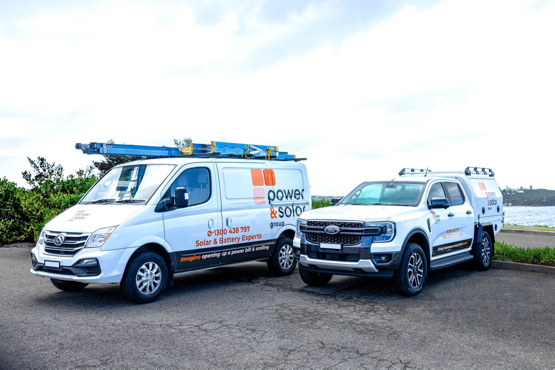 White work van and pickup truck parked on gravel under a cloudy sky