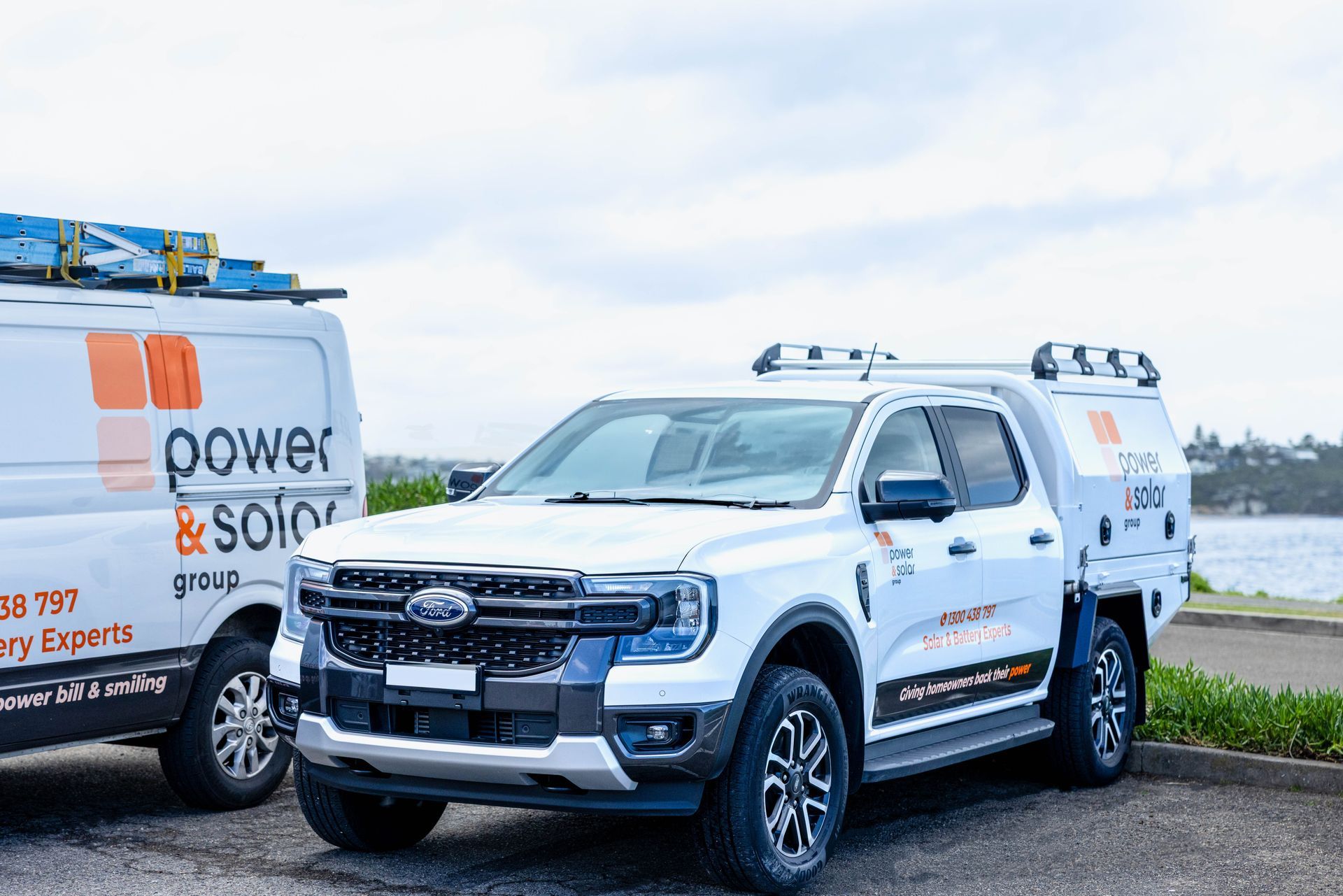 White service pickup truck with roof rack parked beside a Power & Solar van on a roadside.