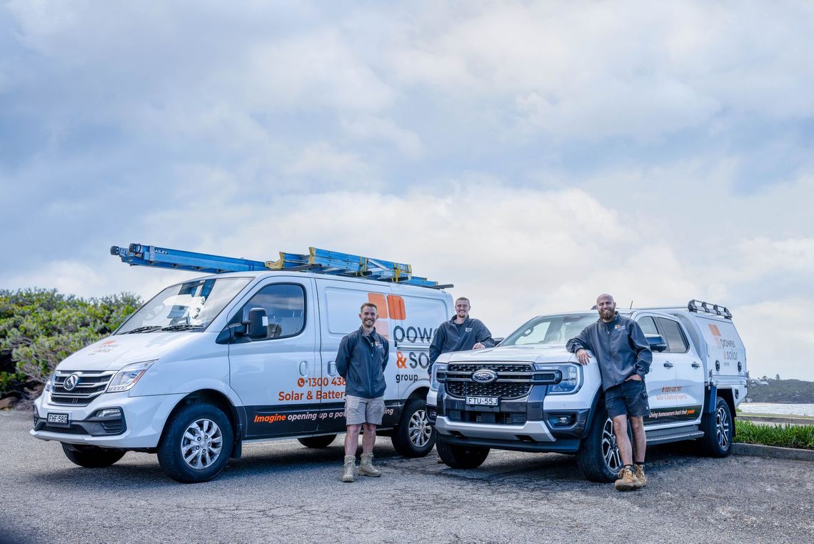 Two white utility vans with ladders parked outdoors, with two people standing beside them under a cloudy sky.