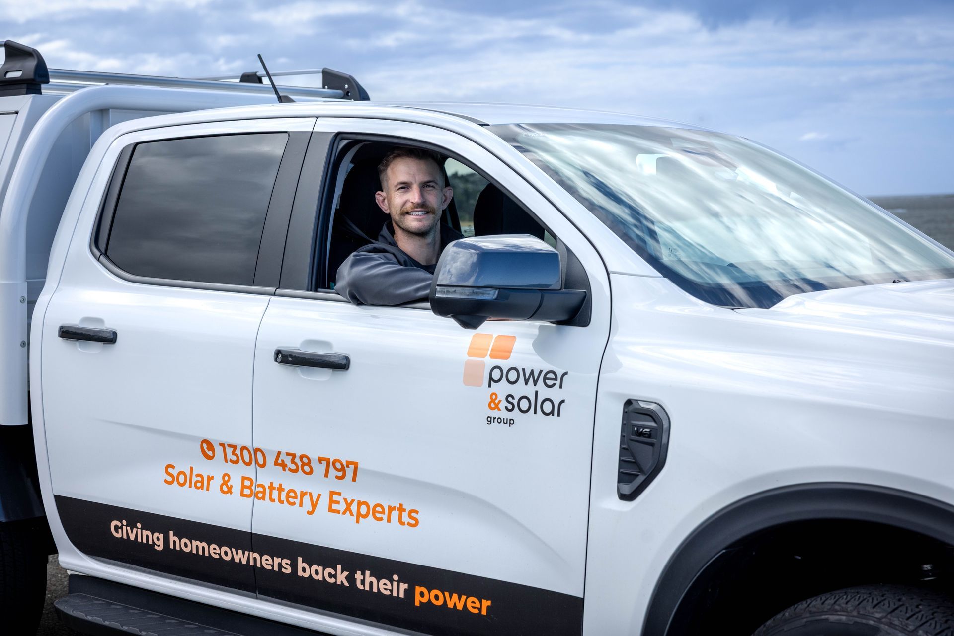 Man in white delivery truck with “Power Solar” branding, smiling through open driver’s window.