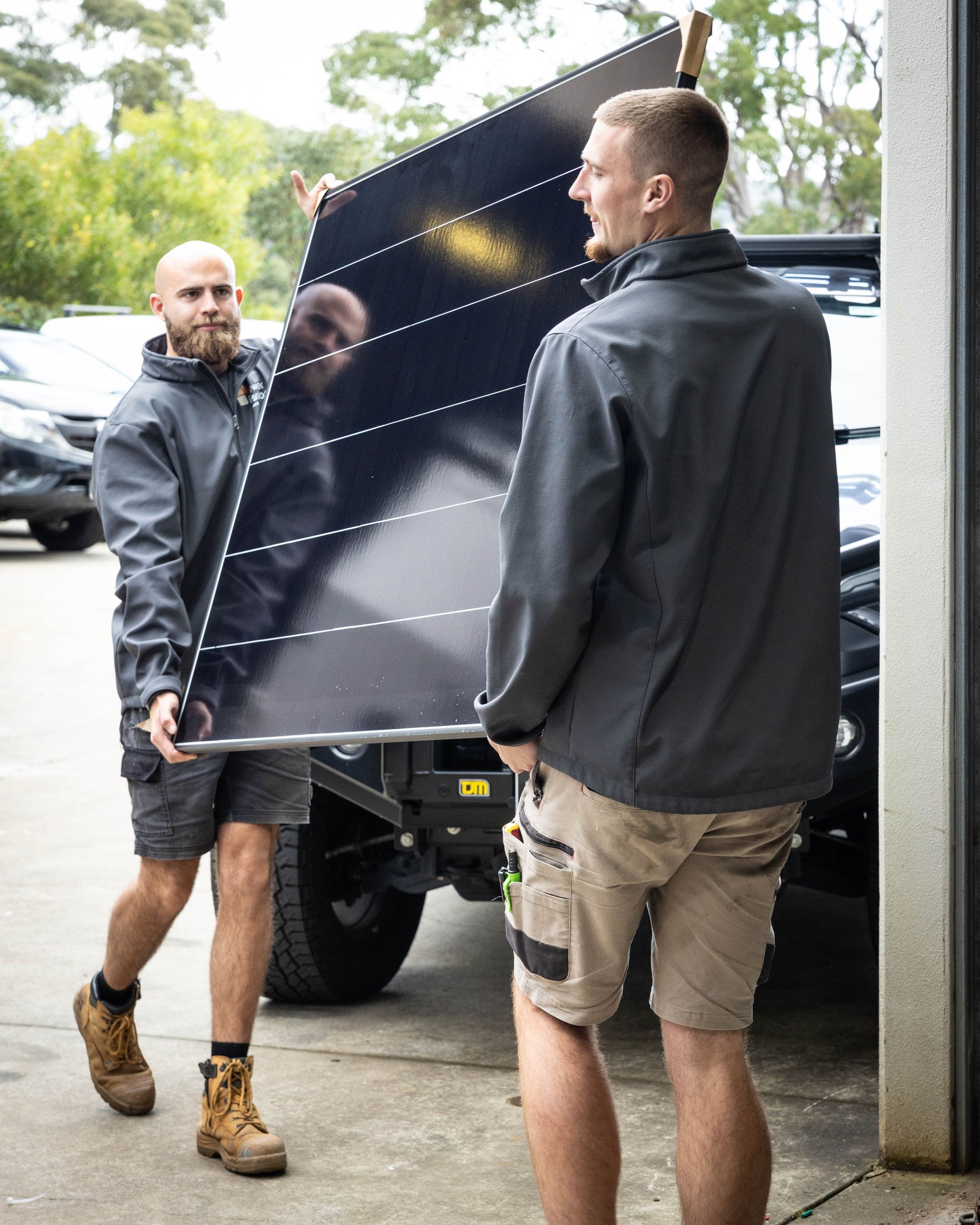 Two workers carrying a large black panel beside a truck in a garage.