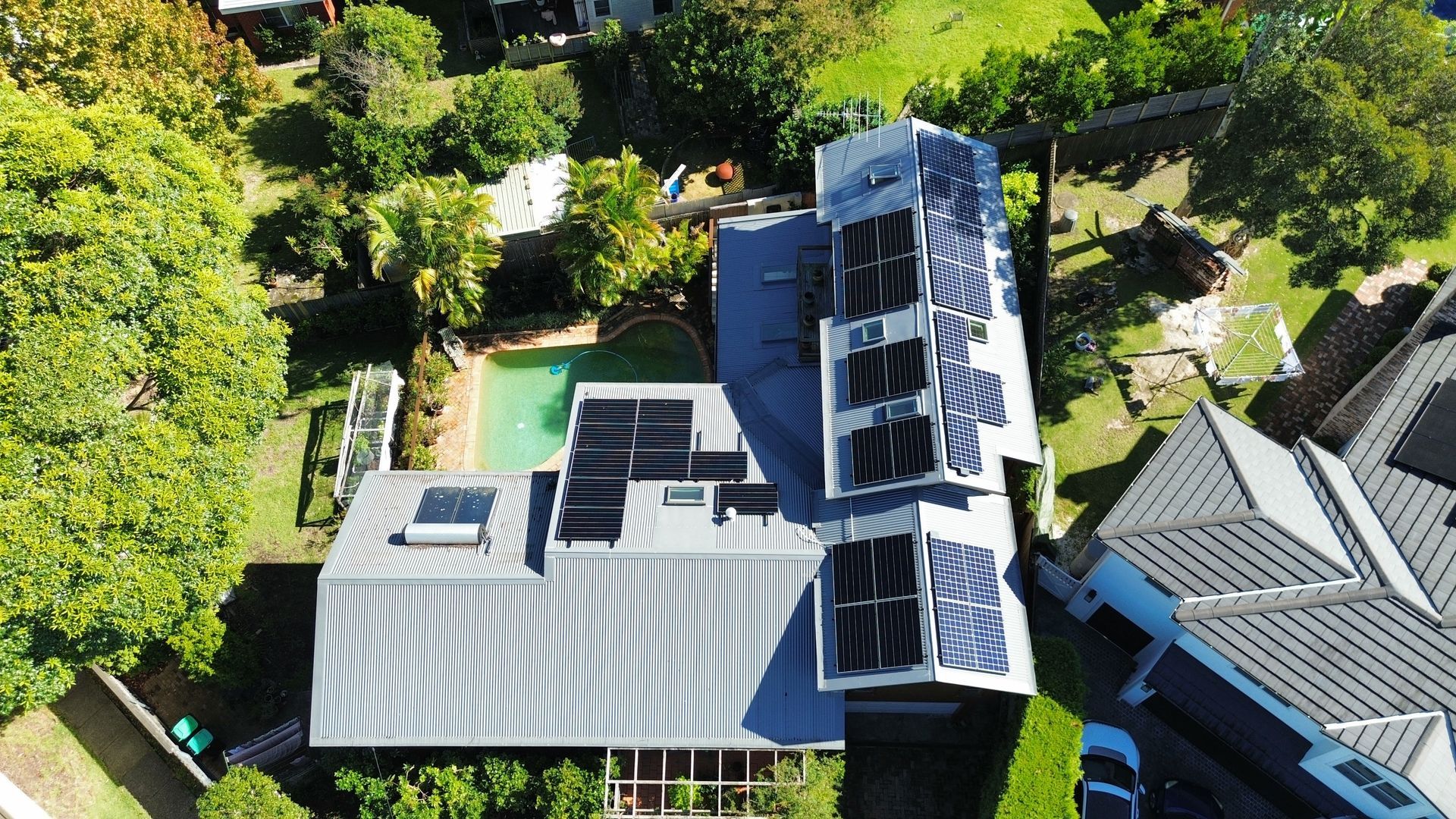 Aerial view of a house roof with solar panels surrounded by trees and neighboring rooftops
