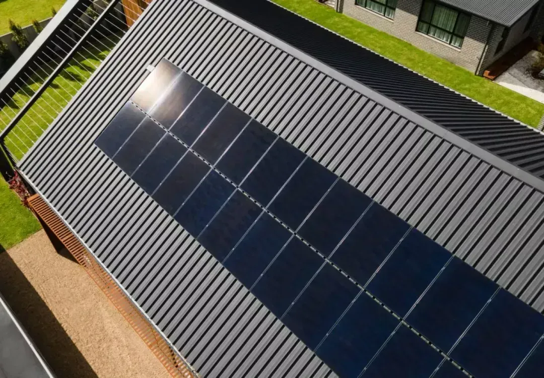 Solar panels installed on a gray metal roof beside a residential yard