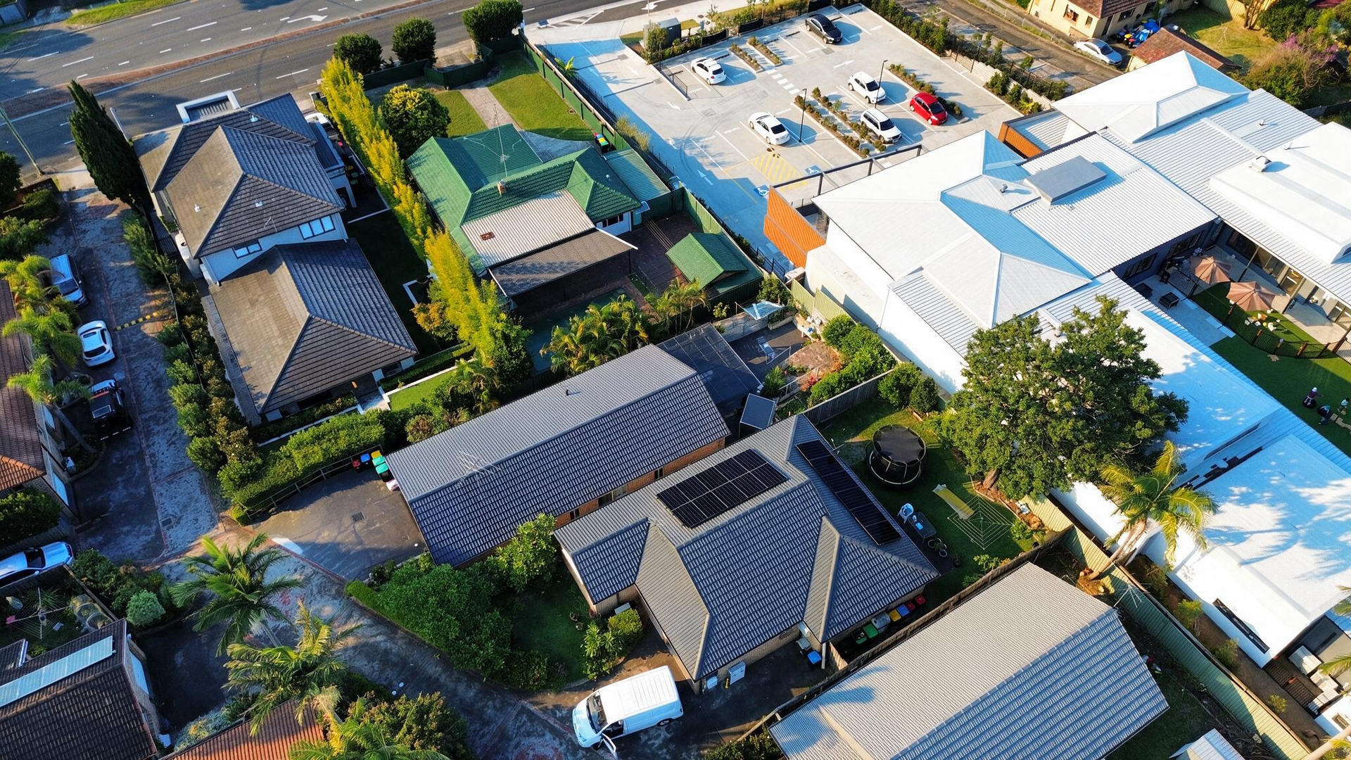 Aerial view of a residential neighborhood with houses, trees, and a swimming pool under bright sunlight.