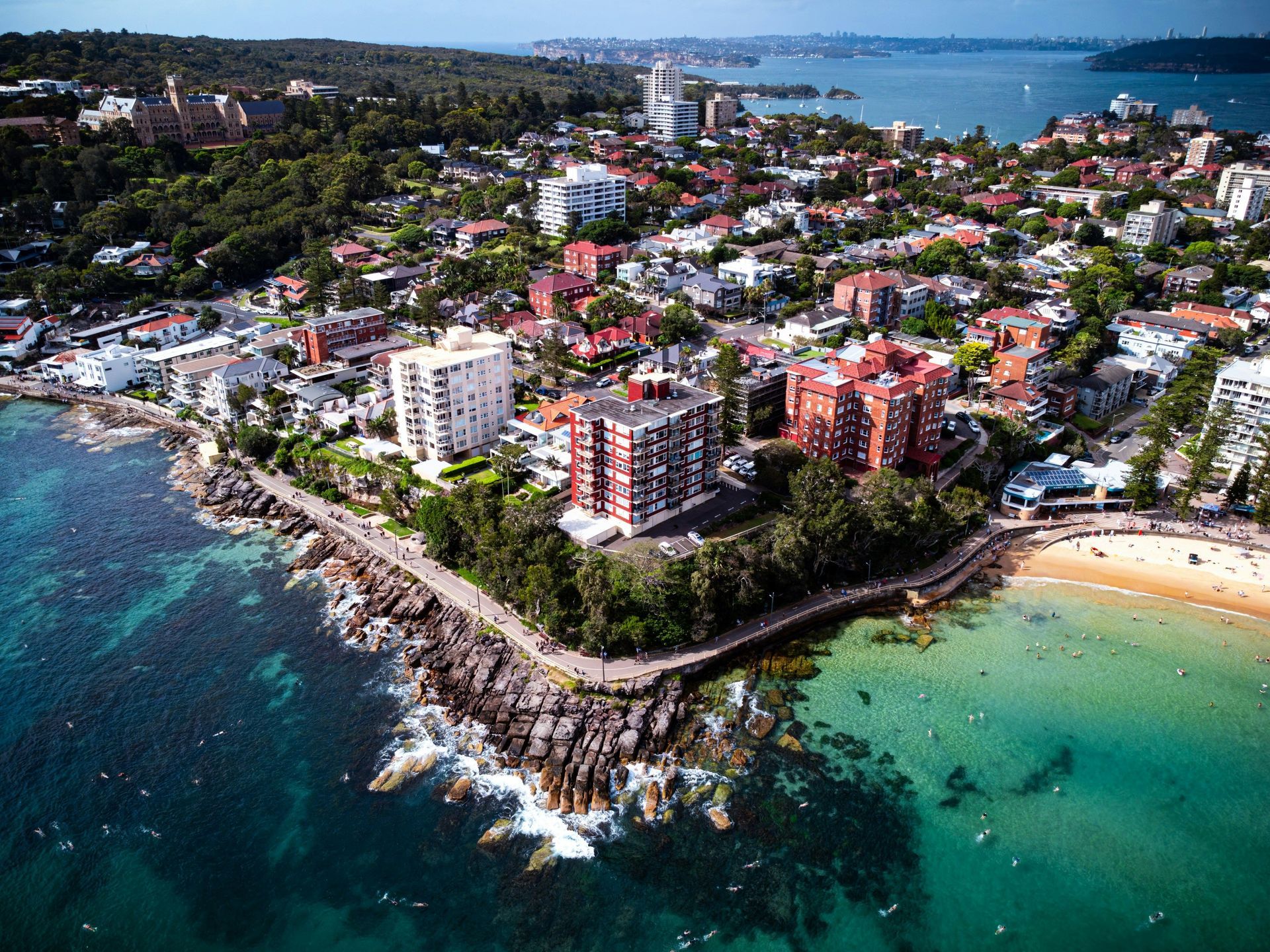 Aerial view of a coastal city with colorful buildings, rocky shoreline, and turquoise water near a beach