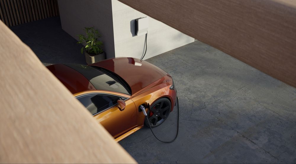Orange sports car charging with a cable in a garage-like indoor space