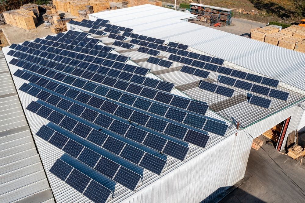 Solar panels installed on a large white-roofed building under construction, with stacked materials nearby