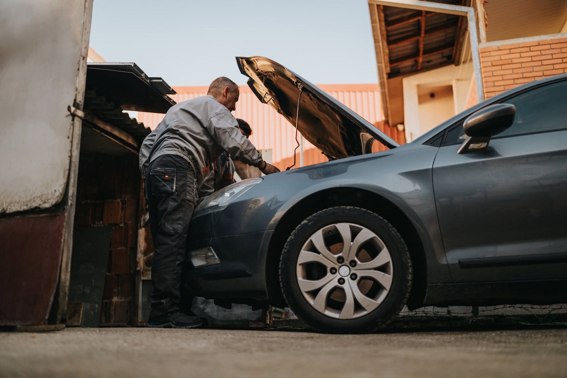 Mechanic working under a raised hood on a gray car in a driveway | Fesserton Auto