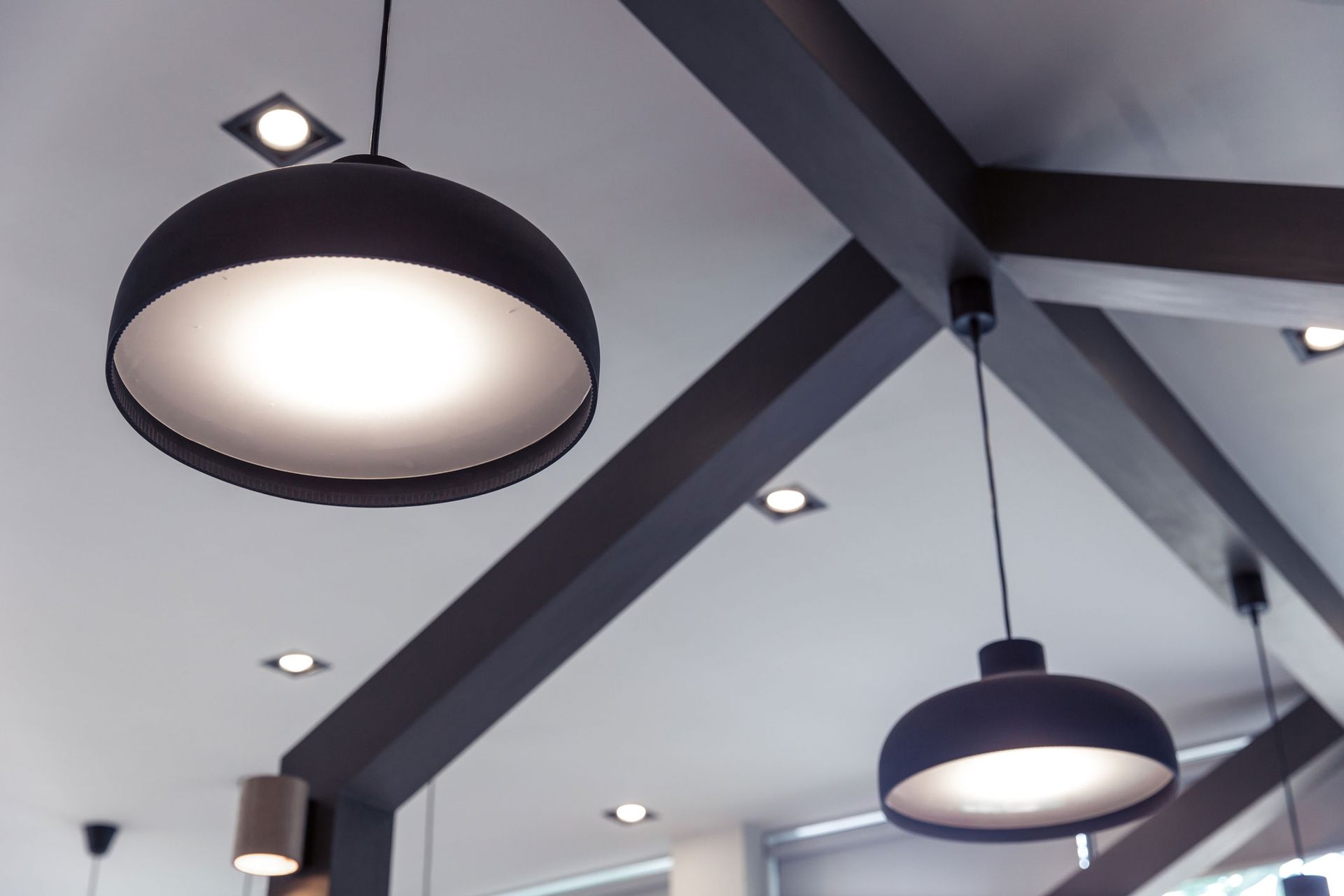 Two black pendant lights hanging from a white ceiling with wooden beams.