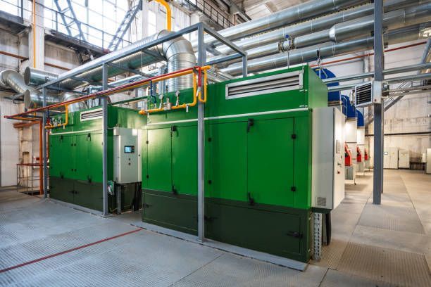 Two large green industrial machines in a factory setting with ventilation pipes. 
