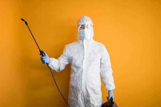 Young man in protective suit disinfects on orange backgrounds
