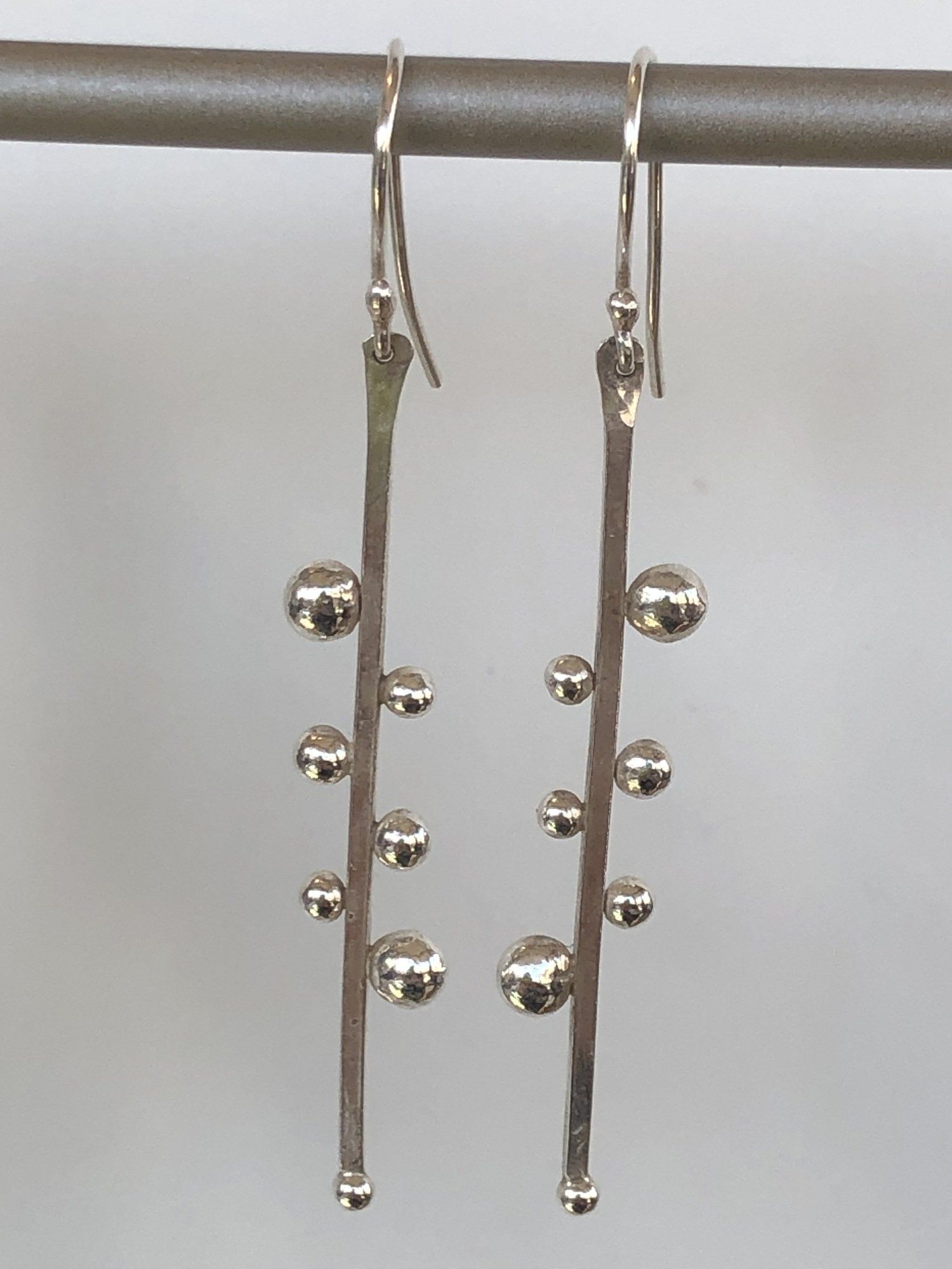 A pair of silver earrings hanging on a metal bar