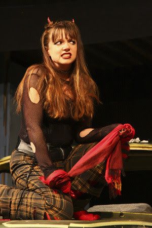 A woman in a devil costume is kneeling down and holding a red scarf.