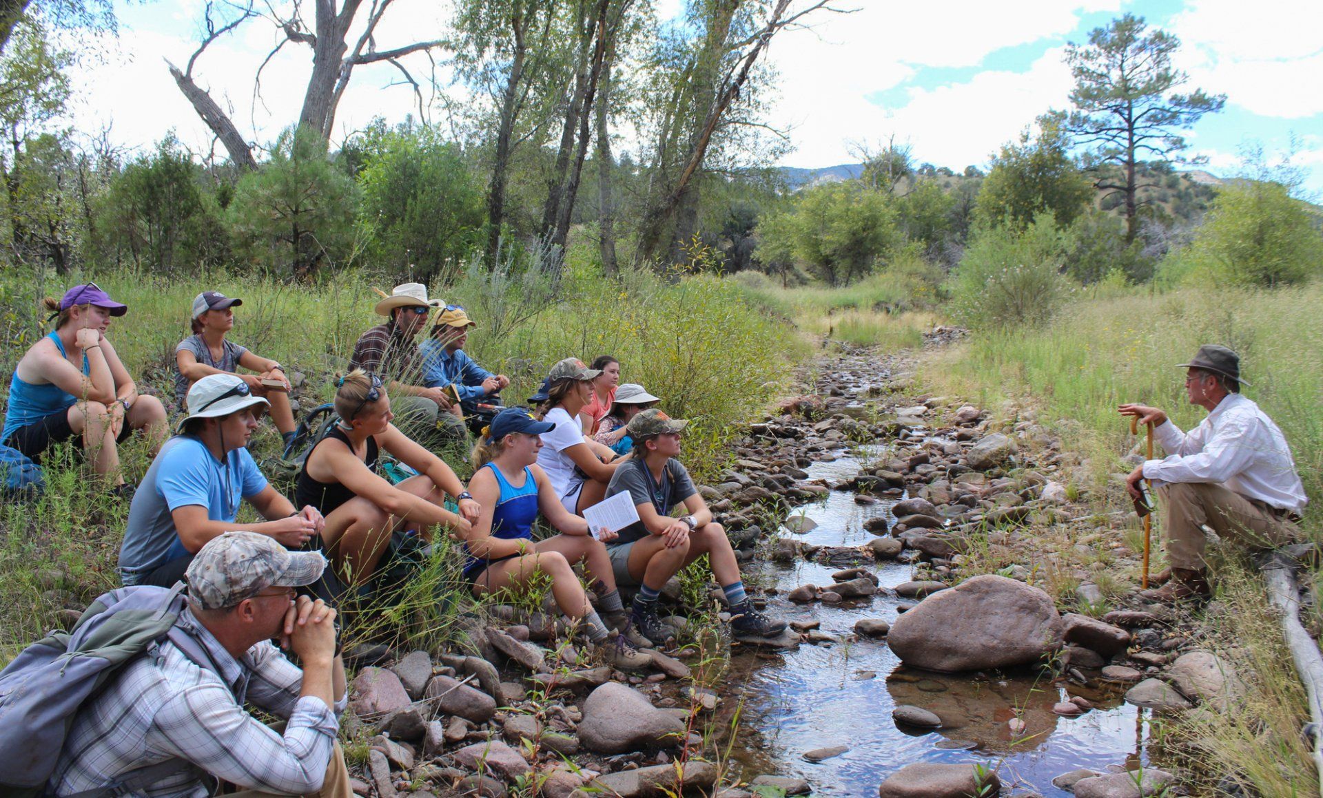 a group of people are sitting next to a stream .