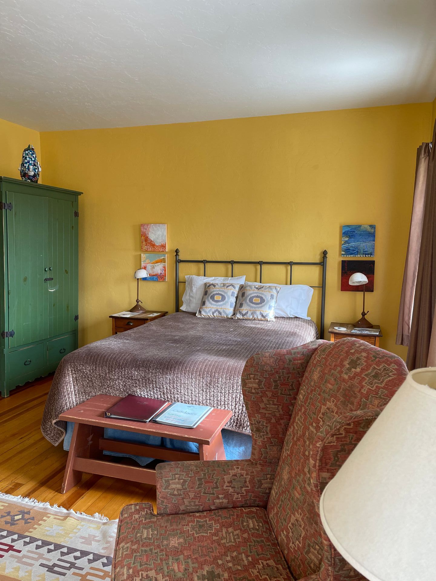 A bedroom with yellow walls , a bed , a chair , and a lamp.