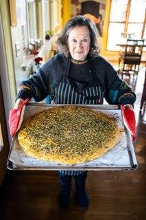 A woman is holding a large pizza on a pan.