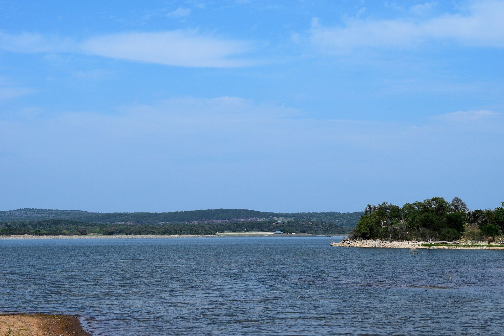 Calm blue bay with a tree-lined shoreline under a clear sky