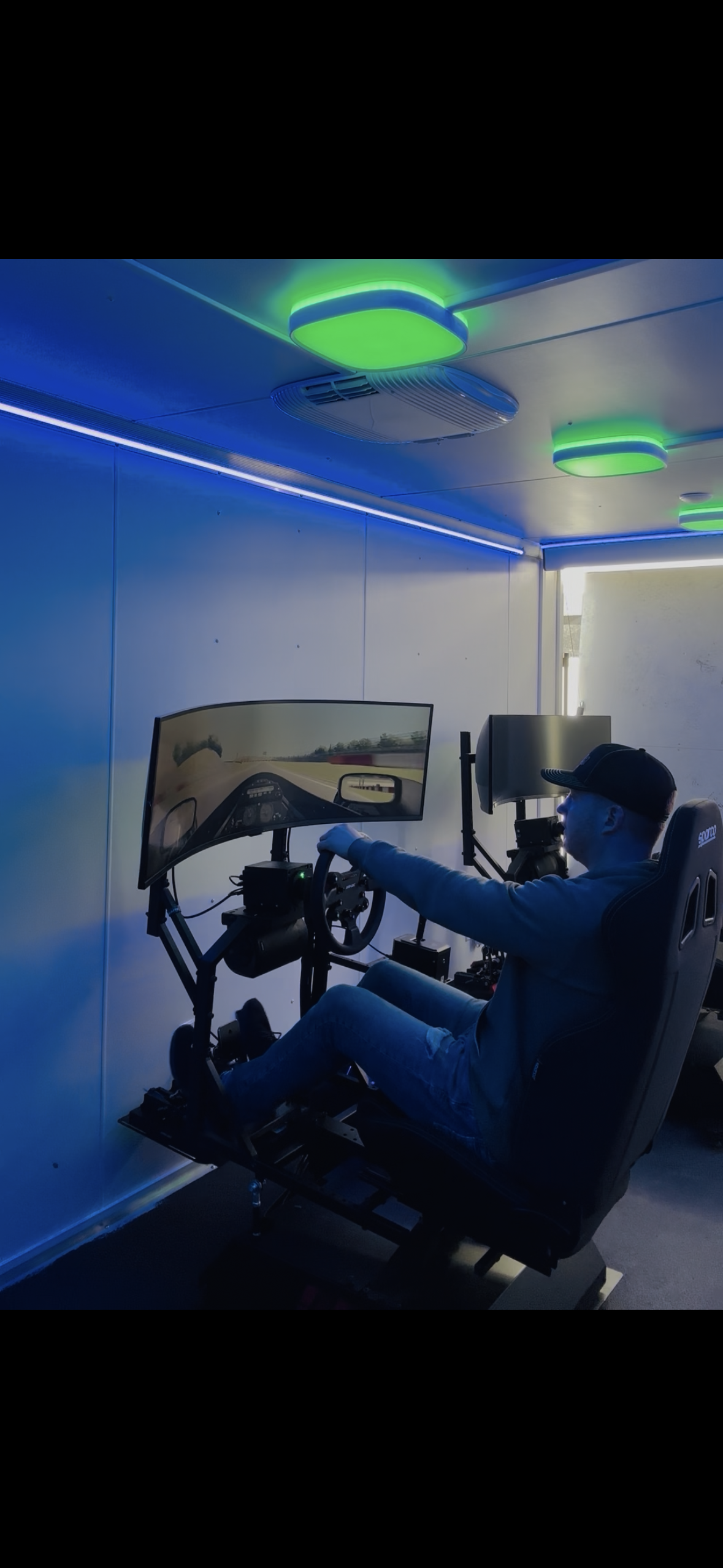 Person using a driving simulator in a dim room with blue and green ceiling lights
