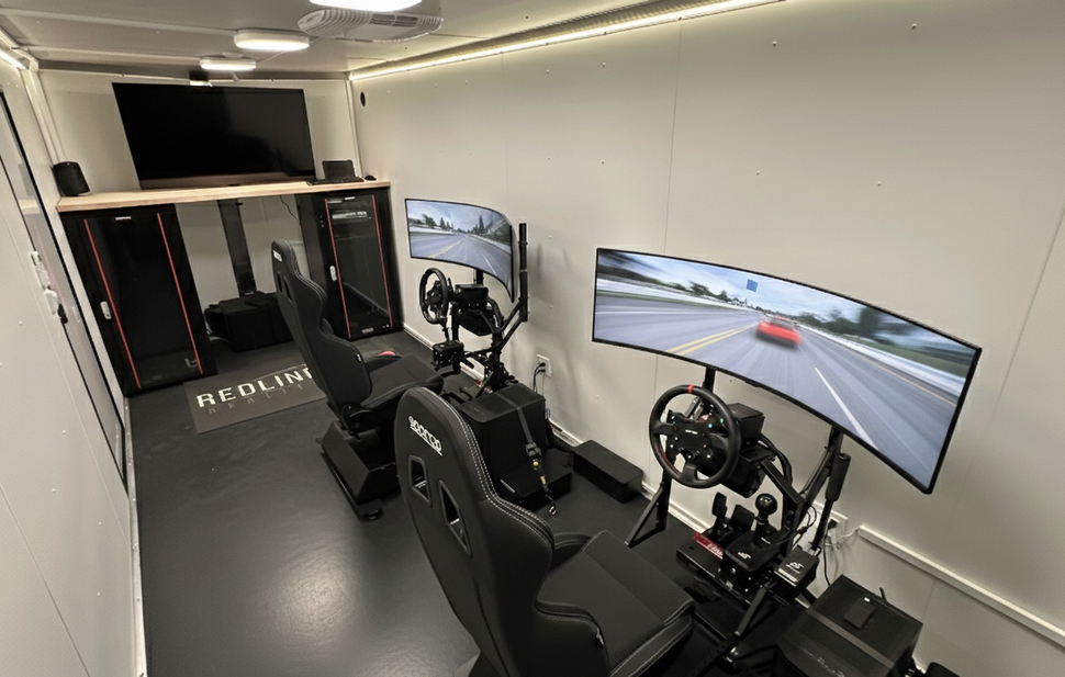 Racing simulator room with two steering setups and wide monitors showing a driving track