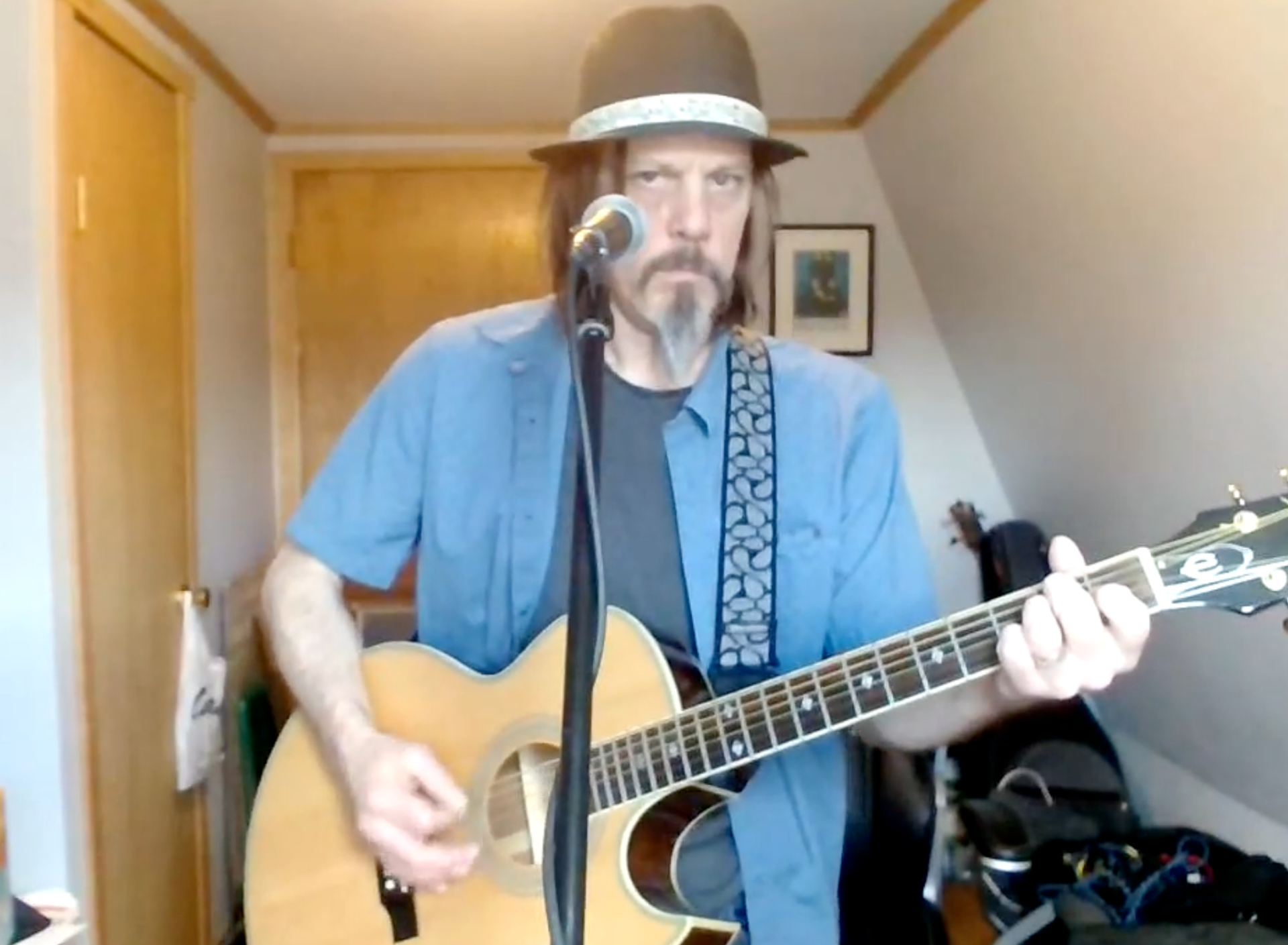 A man with a beard is playing an acoustic guitar in a room.