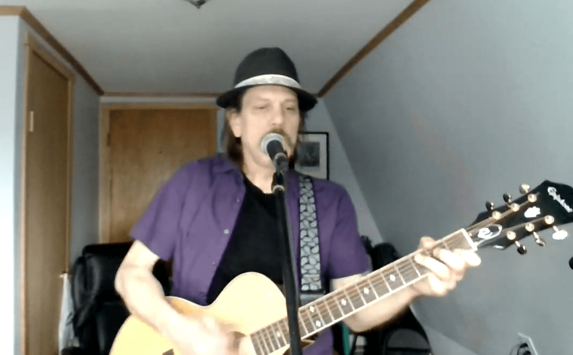A man with a beard is playing an acoustic guitar in a room.