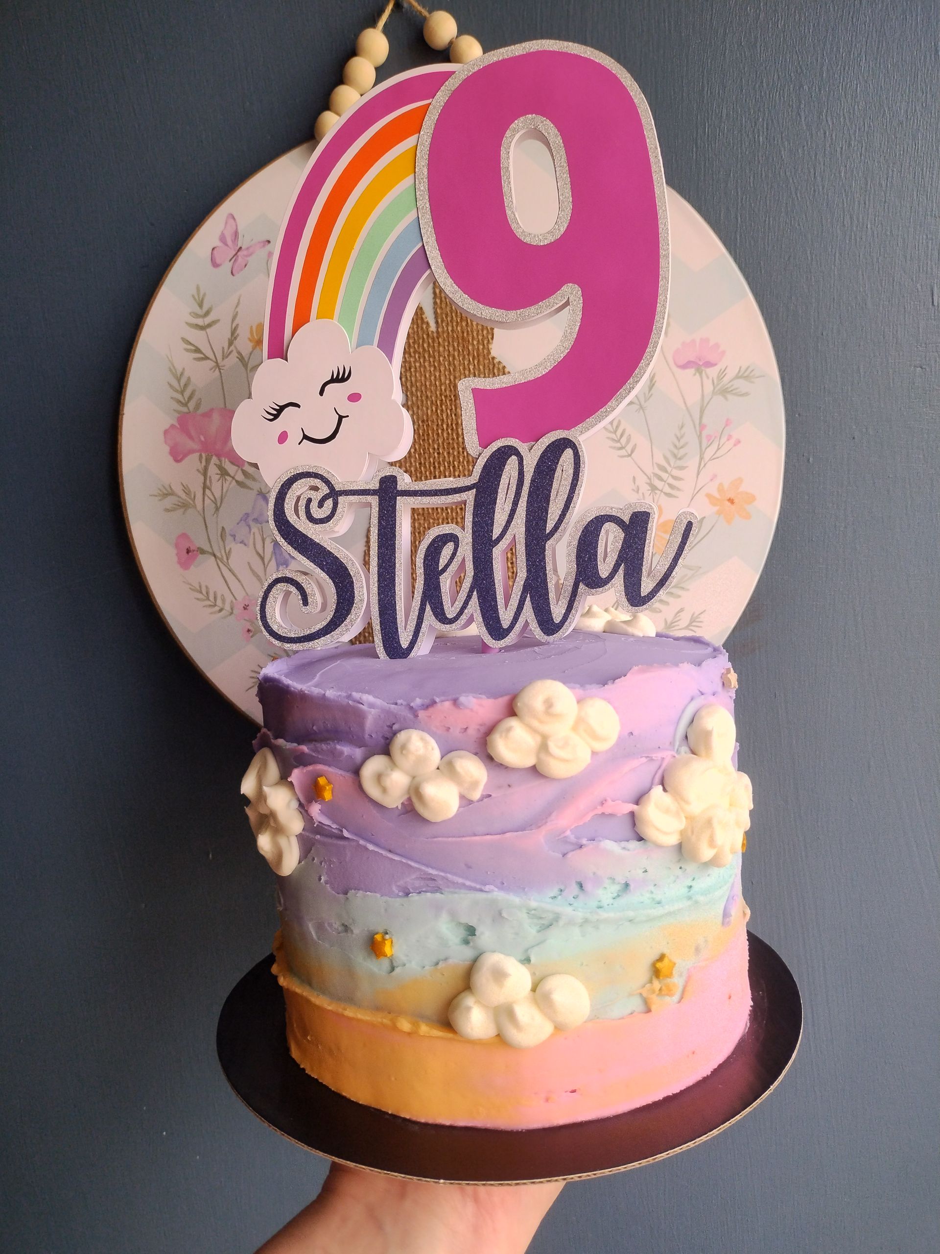 Birthday cake with a rainbow and "9" topper for Stella, decorated with clouds.