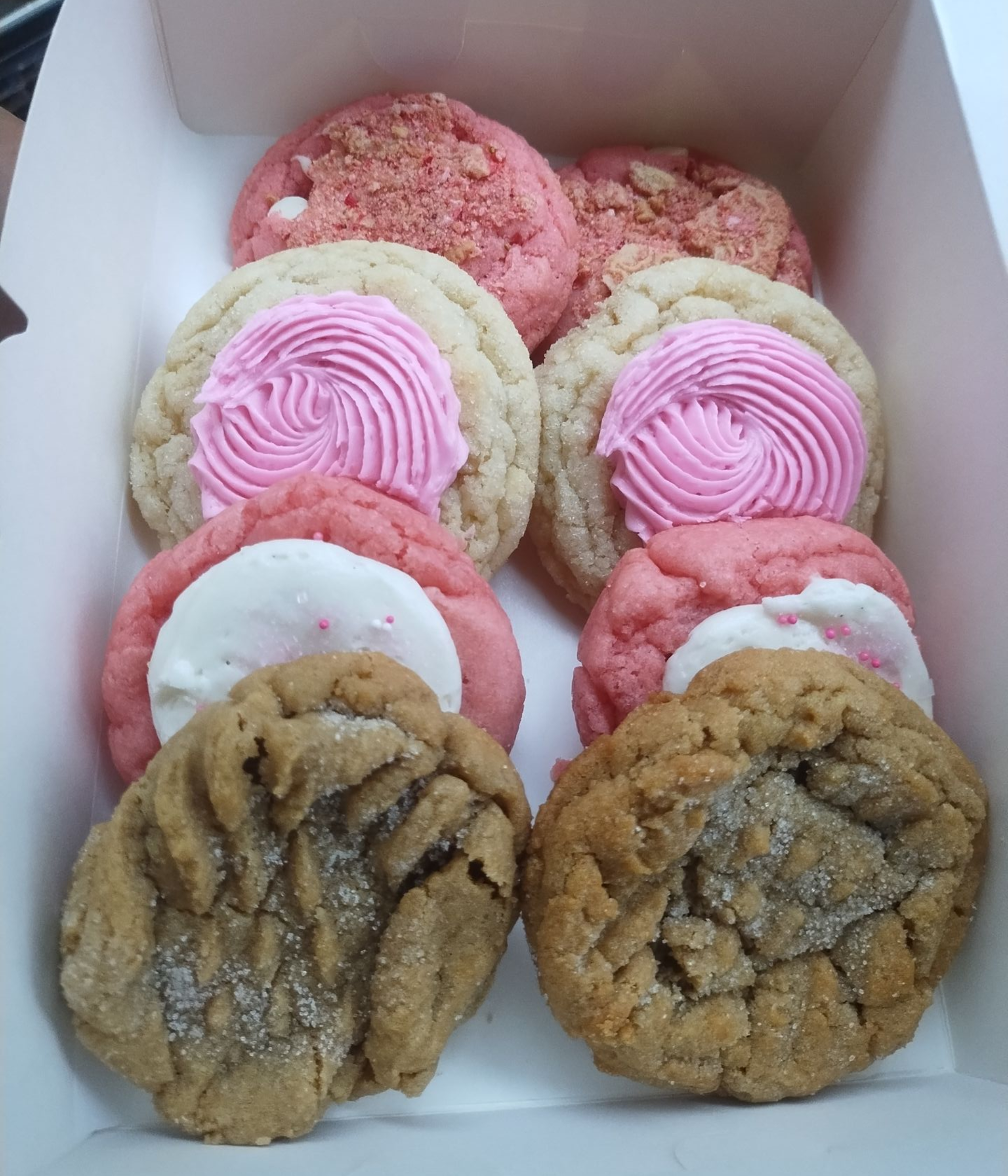 Box of assorted cookies: pink frosted, white frosted, and peanut butter.