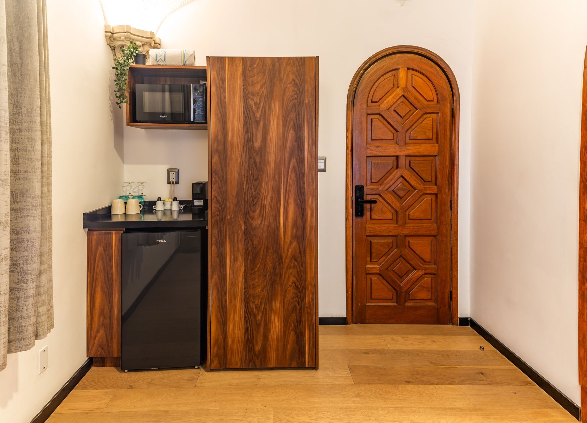 A room with a wooden door , a microwave , and a refrigerator.