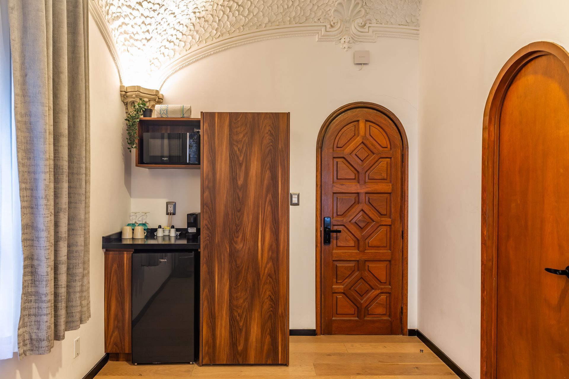 A room with a wooden door , a refrigerator , a microwave and a sink.