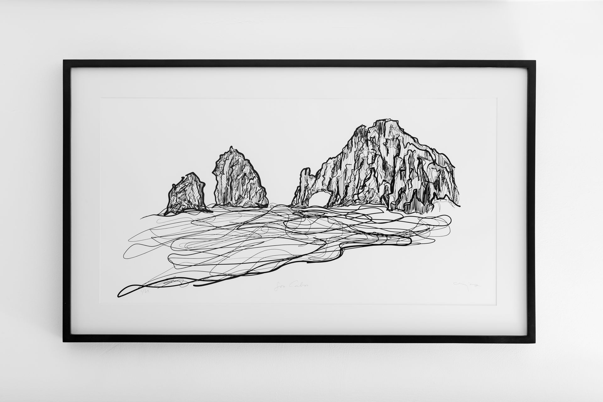 Un dibujo en blanco y negro de una formación rocosa en el océano está colgado en una pared blanca.