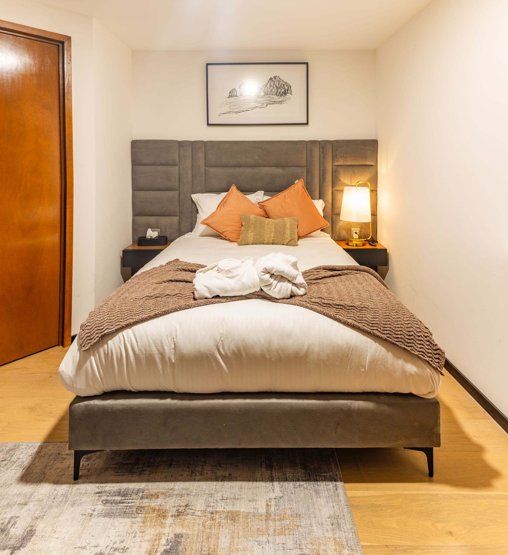 Un dormitorio con cama, mesita de noche, lámpara y alfombra.
