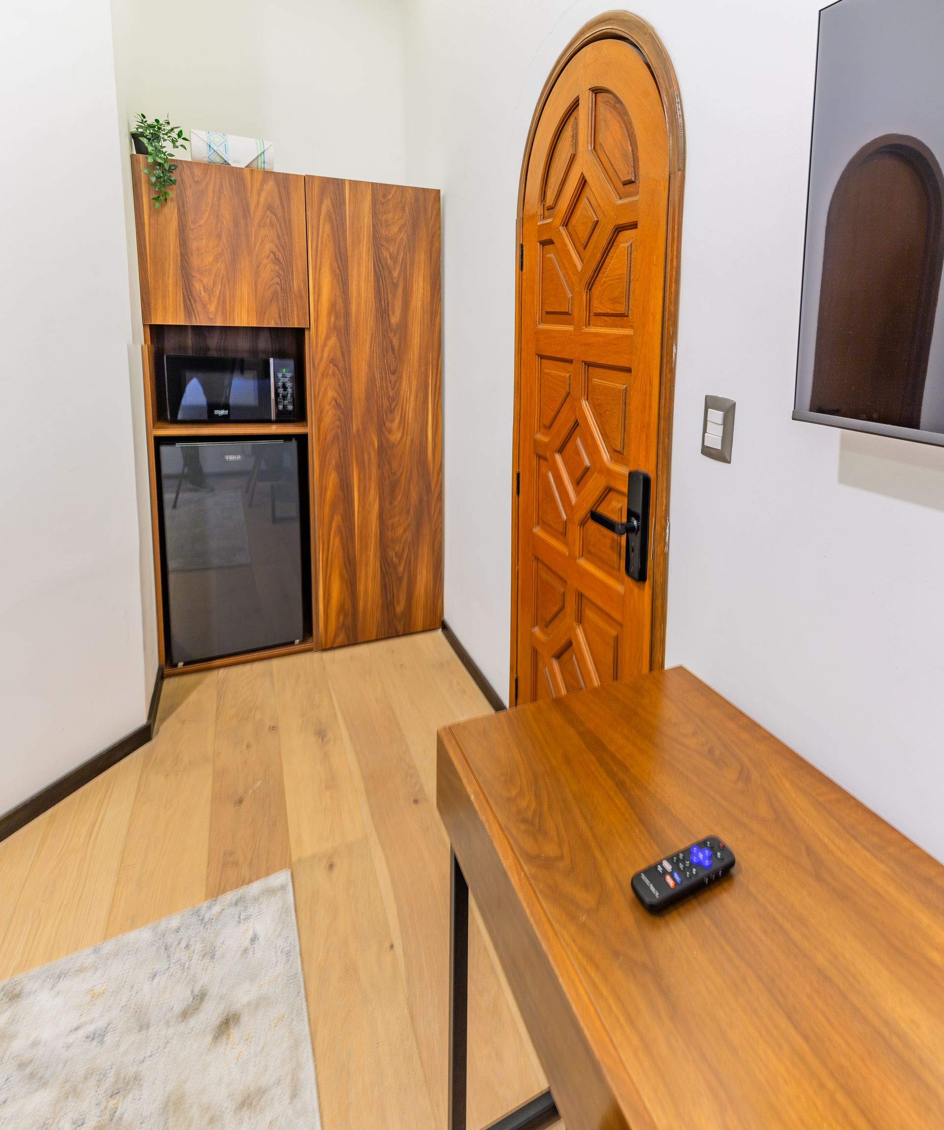 A room with a wooden door and a desk with a remote on it