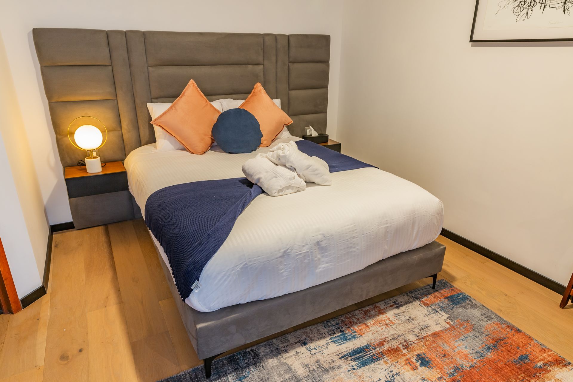 Un dormitorio con cama, mesita de noche, lámpara y alfombra.