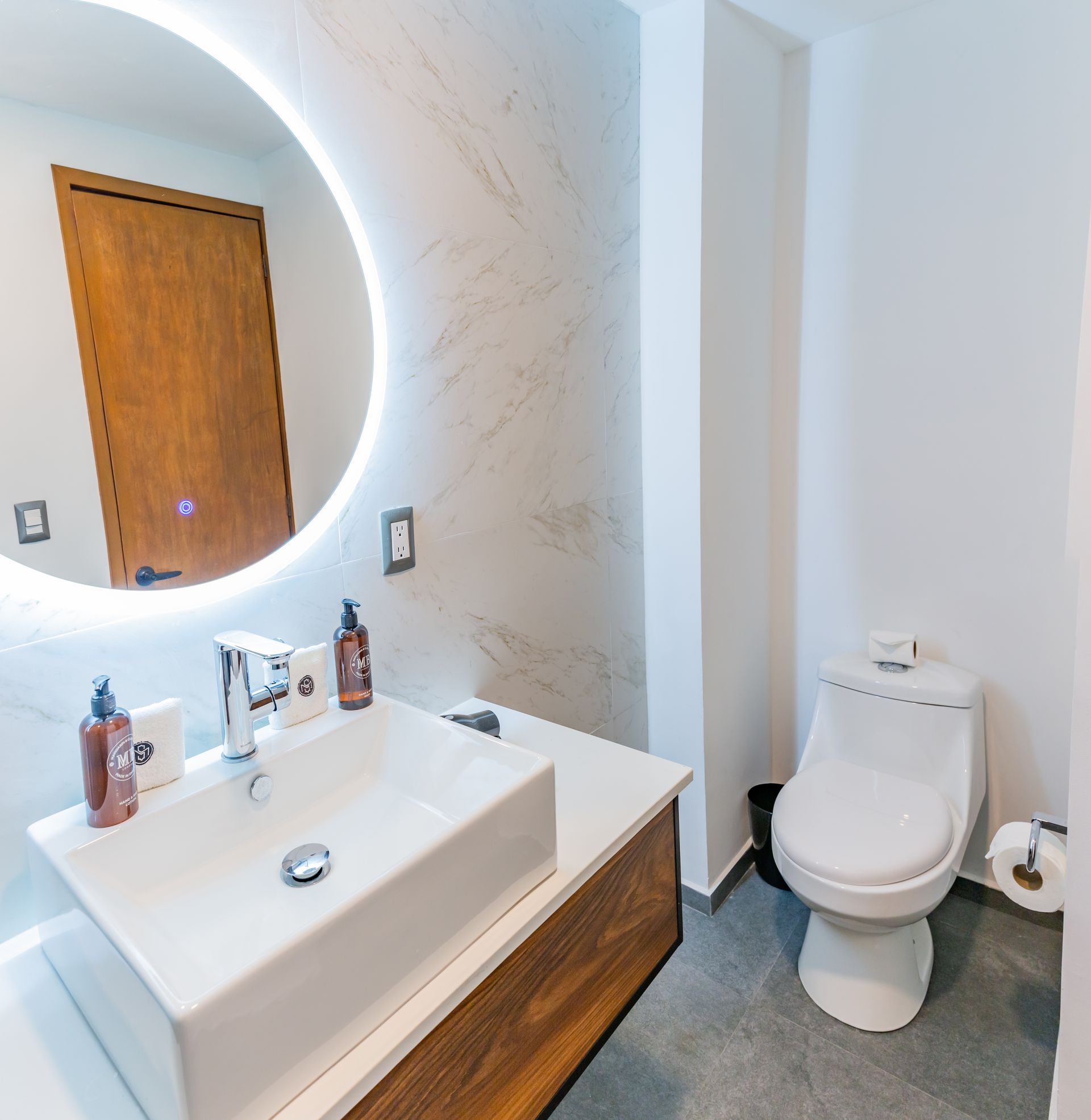 Un baño con lavabo e inodoro y un espejo redondo.