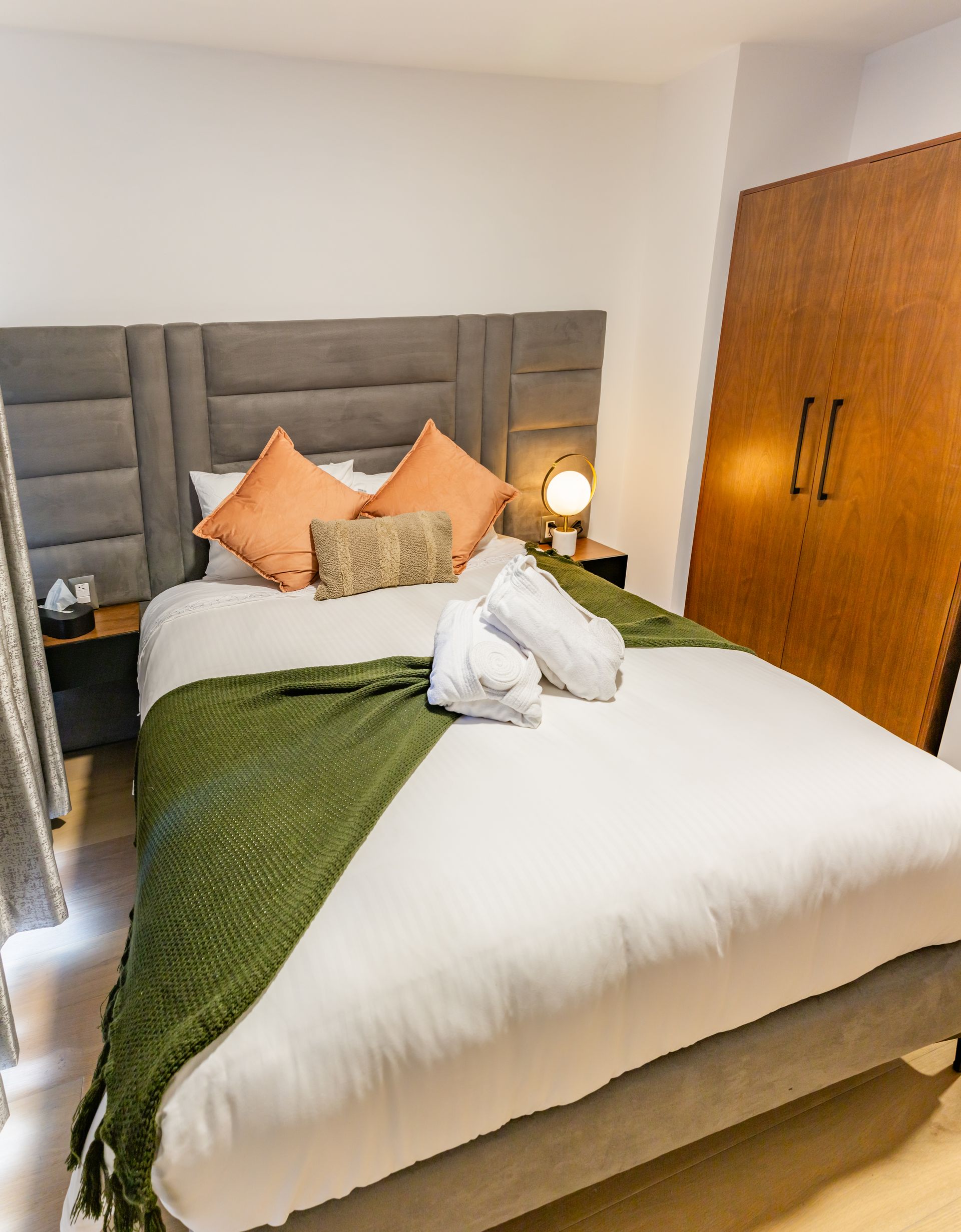 Una cama con una manta verde y almohadas en una habitación de hotel.